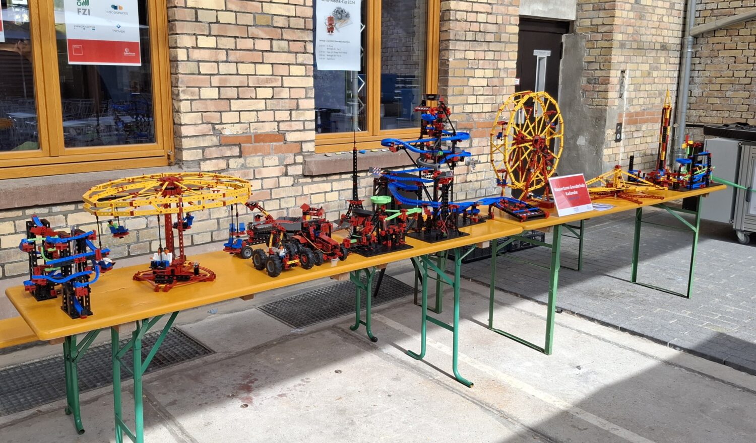 Foto von einem langen Tisch auf dem Lego Modelle ausgestellt sind. Darunter bspw. ein Riesenrad, der Eiffelturm und Baustellenfahrzeuge.